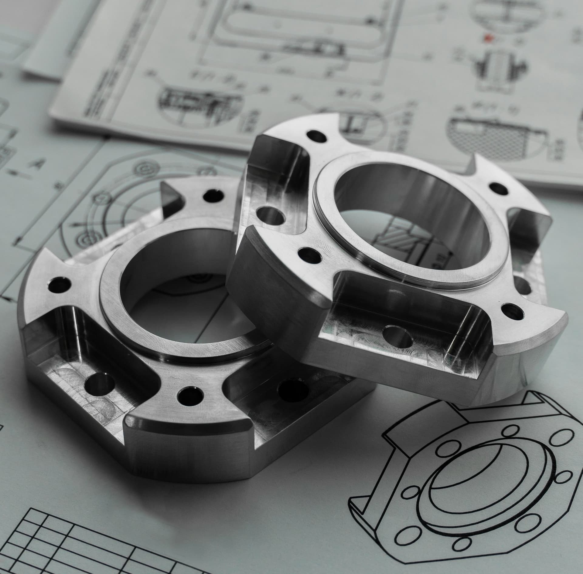 Zwei gefräste Flansche aus Metall liegen auf technischen Zeichnungen
